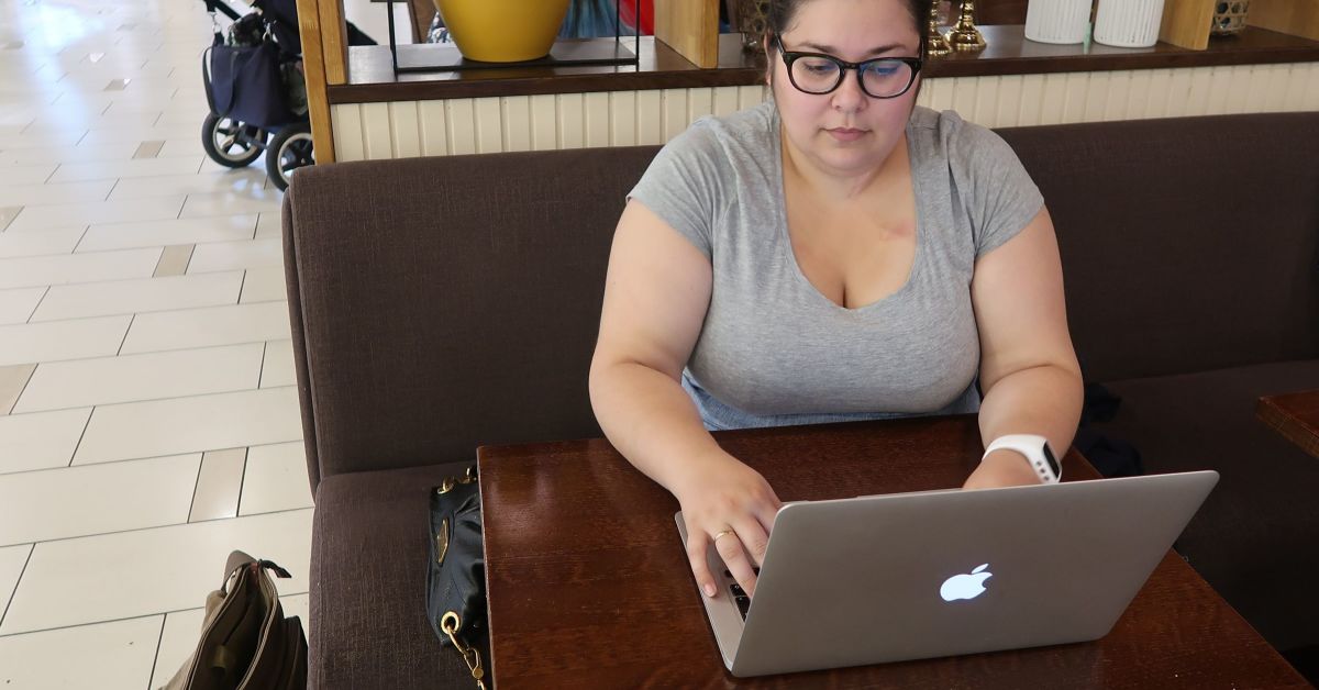 Ung dame sitter og skriver på en laptop på en kafé