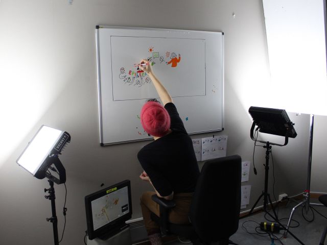 En dame sett bakfra mens hun sitter og tegner på en whiteboardtavle