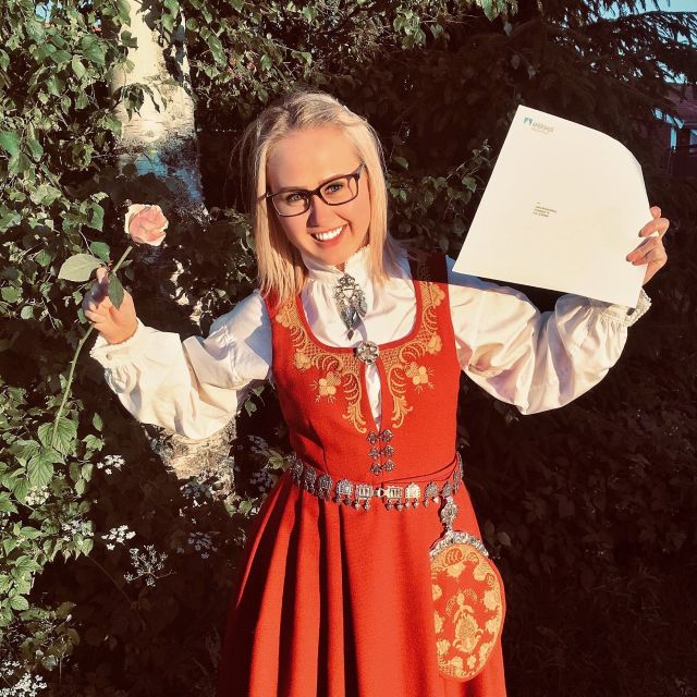 Ung smilende jente i bunad med blomst i hånden